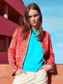A lady wearing a turquoise top, chinos and a red, embroidered jacket