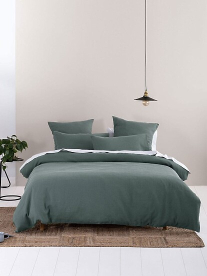 A styled, comfortable bed with green Linen House linen on.