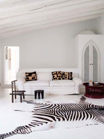 A zebra skin on the floor in a beautifully styled, all-white room next to a white couch