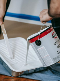 A person pouring white paint into a painters tray